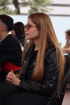 Young woman wearing eyeglasses and a leather jacket at a meeting, focused and thoughtful.