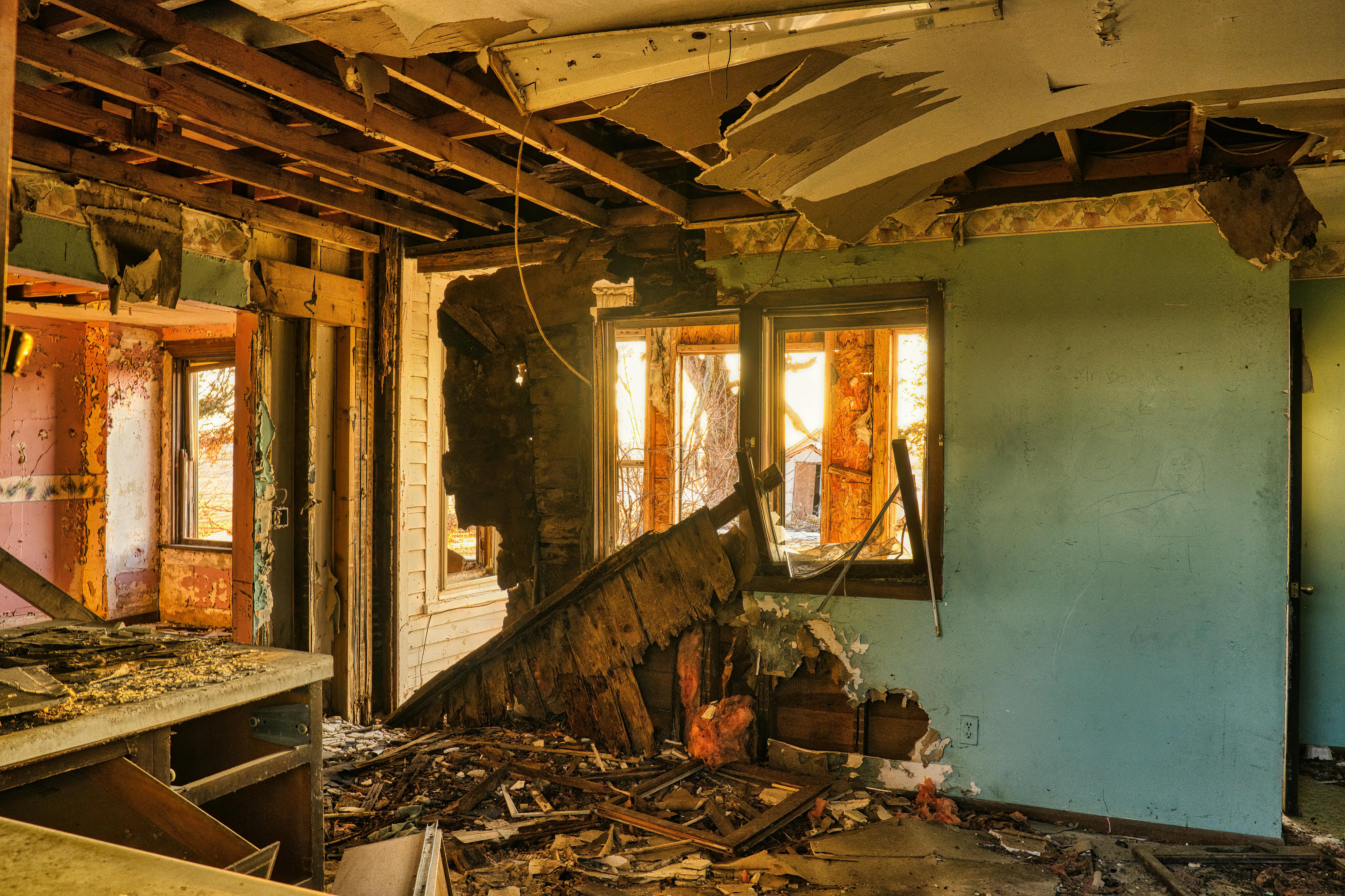Interior of a severely damaged home, showcasing exposed beams, crumbling walls, and debris scattered on the floor, highlighting the need for major repairs and renovation expertise.