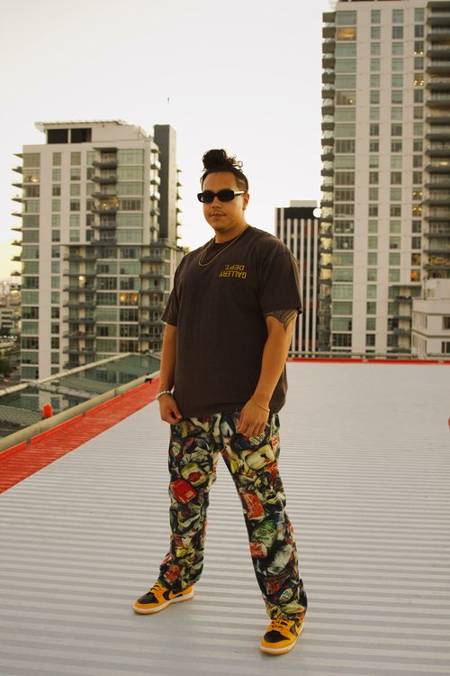 Free Stylish man in sunglasses posing on a city rooftop during sunset with a modern skyline backdrop. Stock Photo