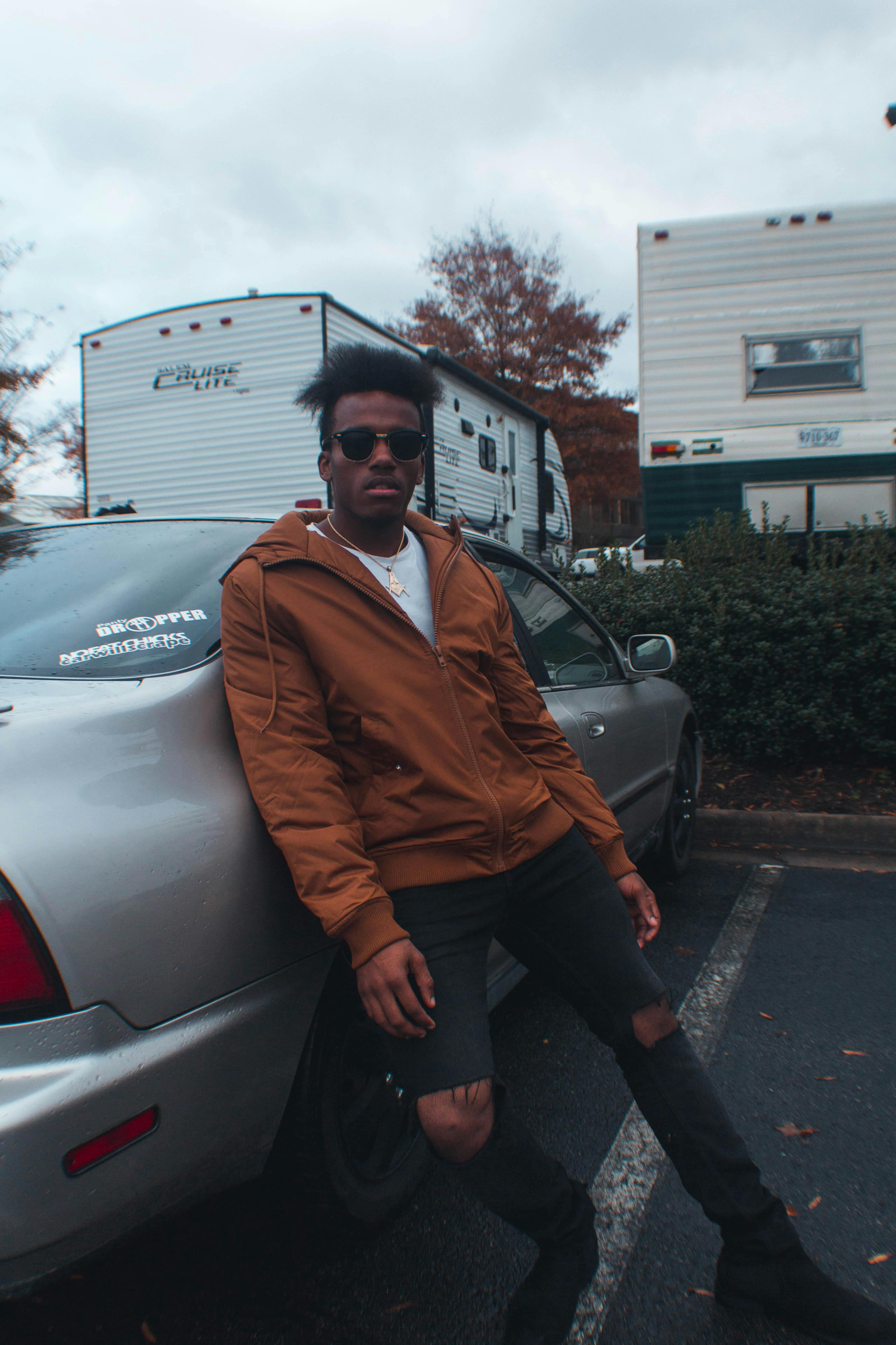 城市停车场里，一名穿着休闲装的男子靠在一辆汽车上，周围停满了房车