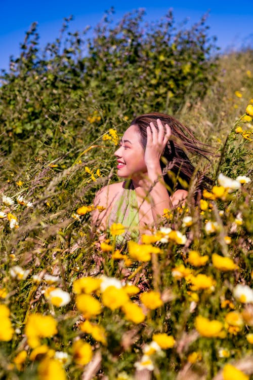 Young Woman Sitting on a Meadow with Flowers and Smiling 