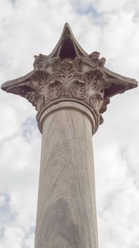 Low angle view of a historic marble column in Istanbul, showcasing intricate carvings against a cloudy sky.
