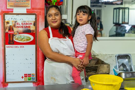 A mother holding her daughter in a local eatery near a 'Menu del Dia' sign.