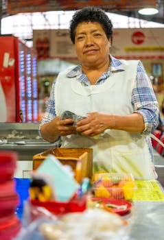 Smiling woman vendor in a bustling market setting wearing an apron, preparing food.
