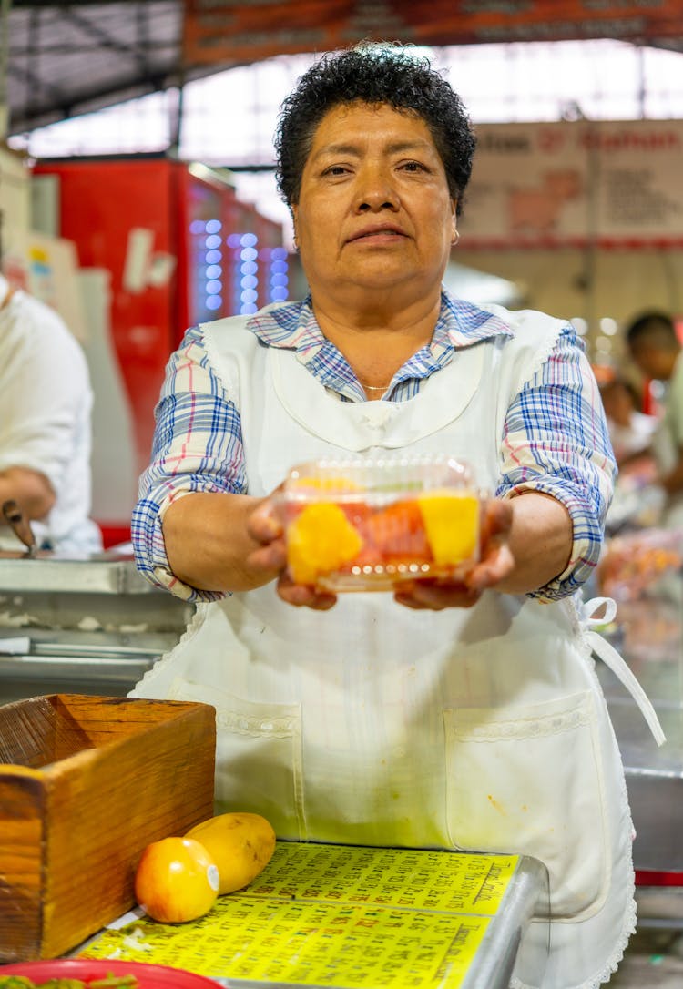 Woman In A Kitchen Apron Holding A Container With Fruit 