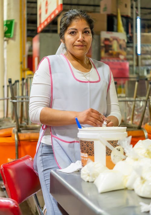 Woman in a Kitchen Apron Standing at a Table with a Bucket and Bags 