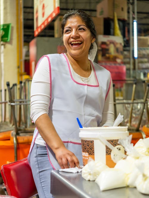 Woman in a Kitchen Apron Standing at a Table with a Bucket and Bags 