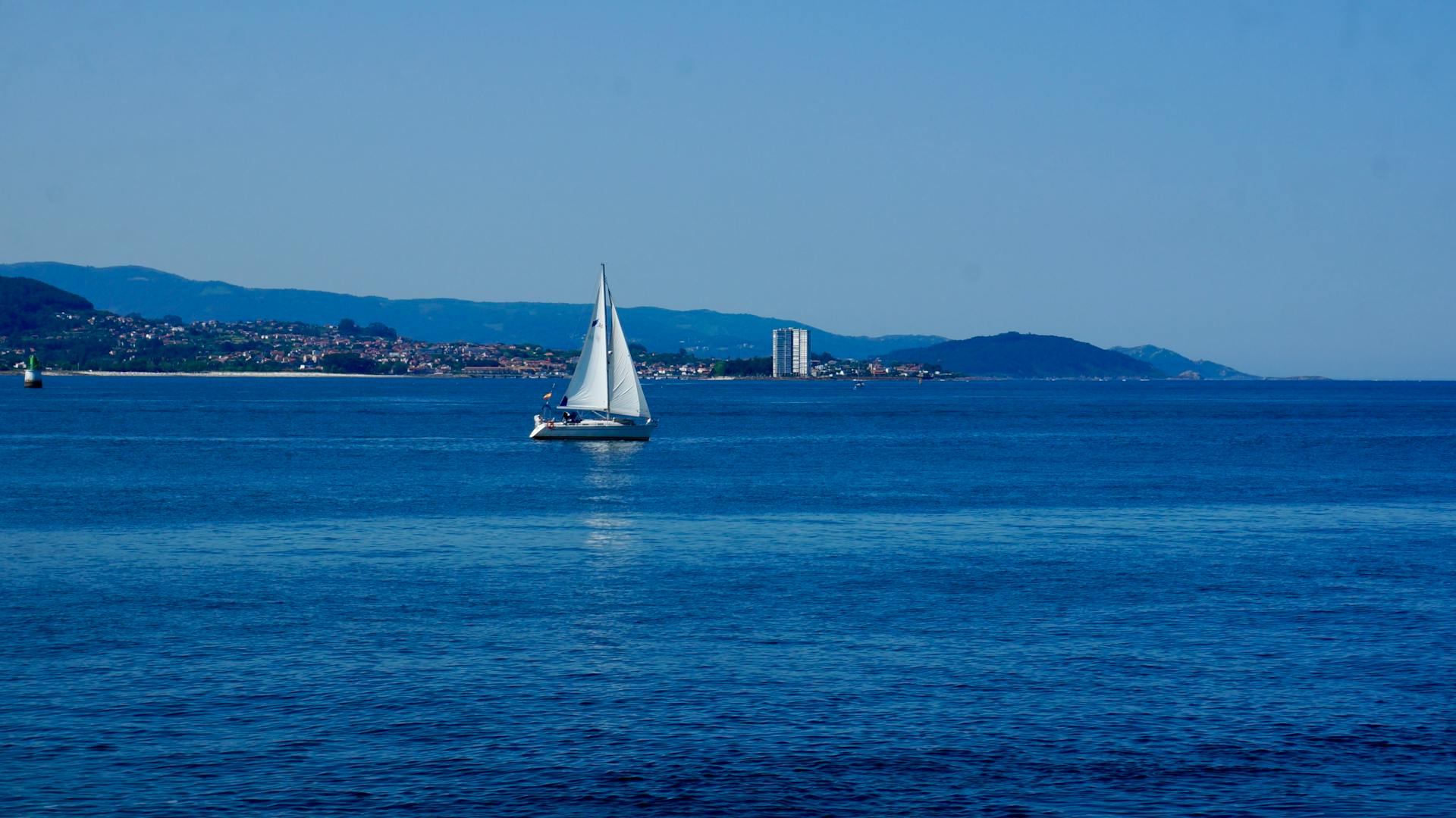 A tranquil scene of a sailboat gliding across the blue waters of Vigo Bay, Spain.