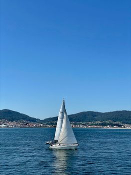 A peaceful sailboat on serene waters against the backdrop of Vigo, Spain, under a clear blue sky.