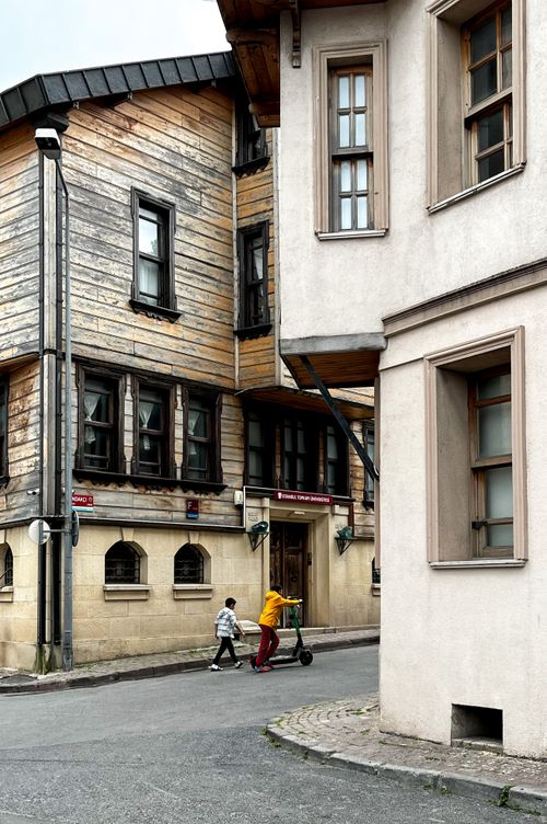 Free An urban street in Istanbul's Balat neighborhood with wooden architecture and people passing by, showcasing Turkish culture. Stock Photo