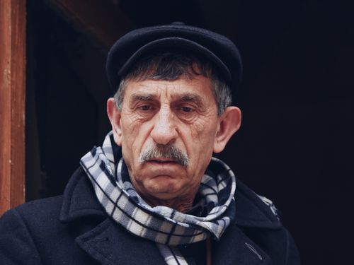 Free Close-up portrait of a senior man in a coat and scarf, looking thoughtful. Stock Photo