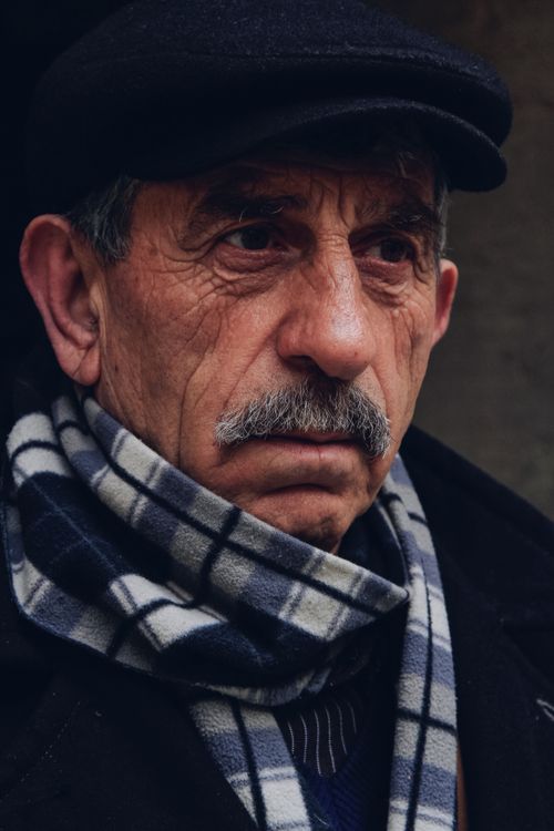 Free Portrait of an elderly man wearing a black cap and warm plaid scarf, showcasing a thoughtful expression. Stock Photo
