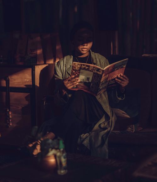 Free A woman in a dimly lit room reading a magazine with shadows cast on her face. Stock Photo