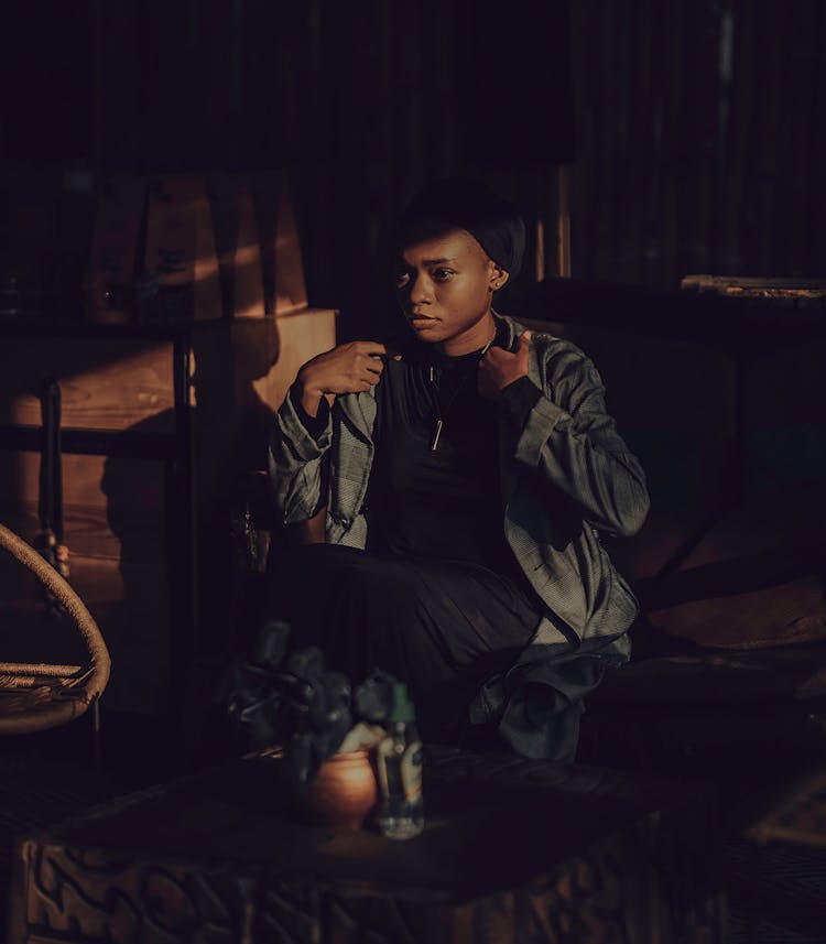 Young Woman Sitting On A Sofa In A Dark Room With The Sun Shining On Her Face 