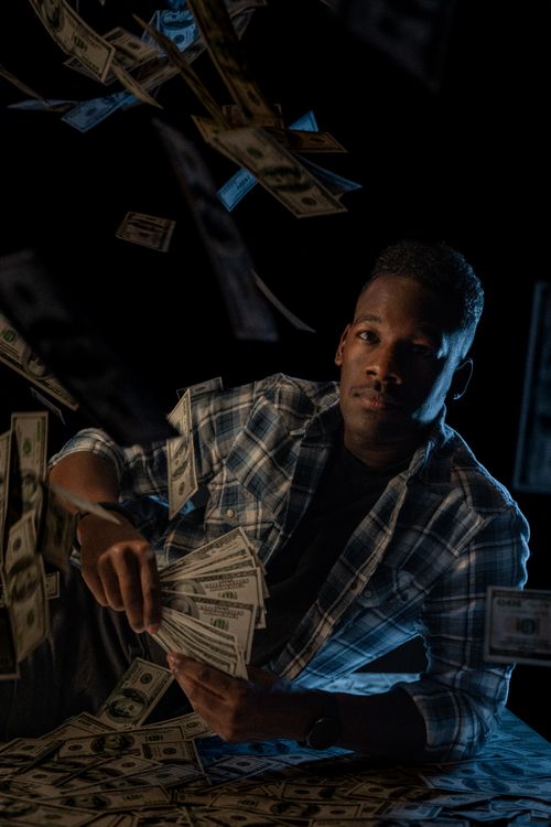 Free Man in a plaid shirt holding cash, surrounded by floating money in a studio setting. Stock Photo