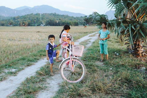 Children with Bicycle on Dirt Road near Rural Field