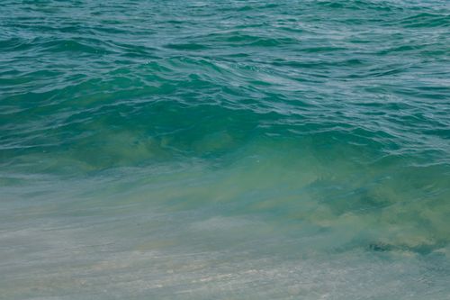 Free Tranquil turquoise ocean waves gently rolling onto a sandy beach on a sunny summer day. Stock Photo