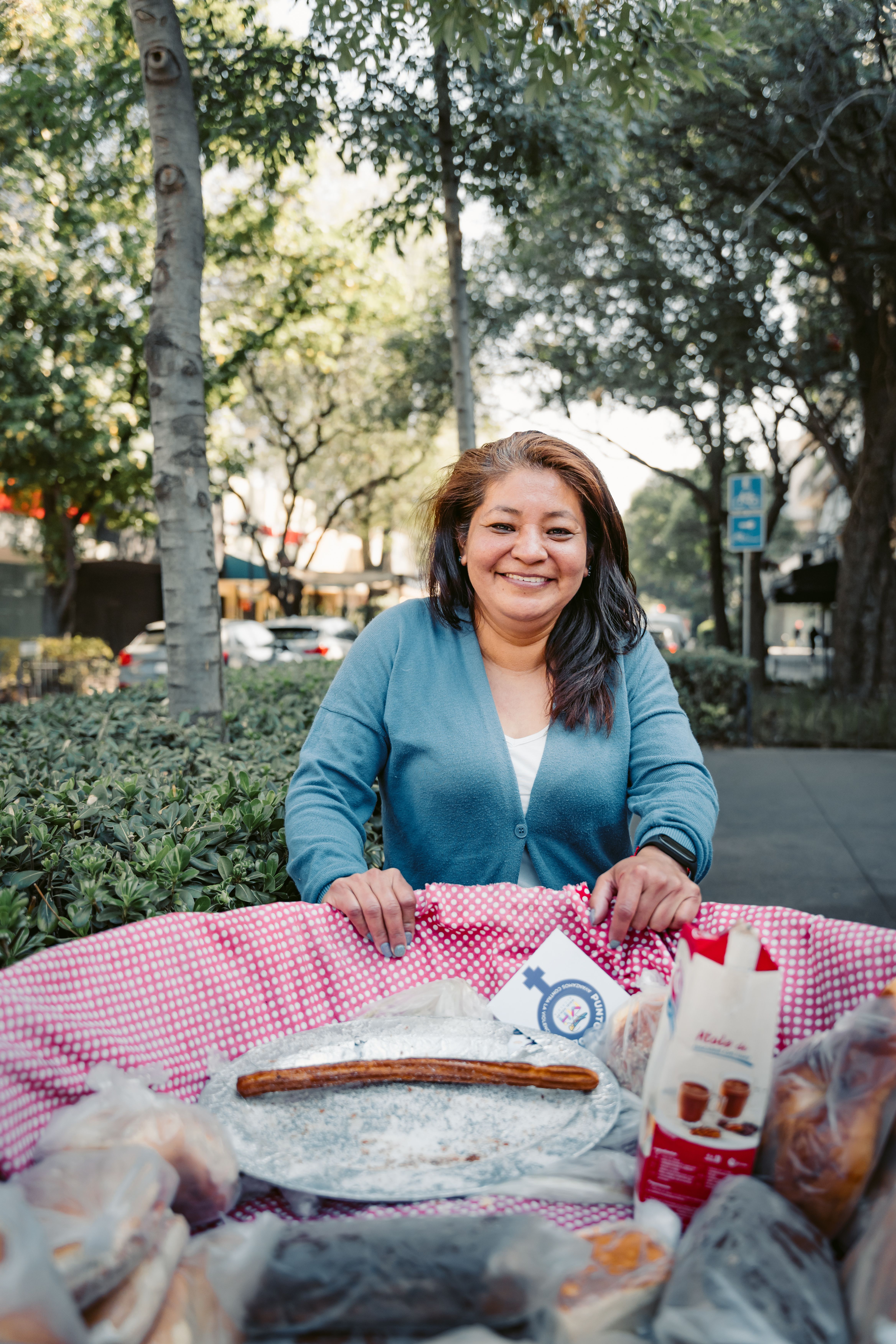 Smiling woman street vendor with baked goods in urban park setting in Mexico City.