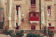 View of historic Valletta street with closed umbrellas and red balconies.