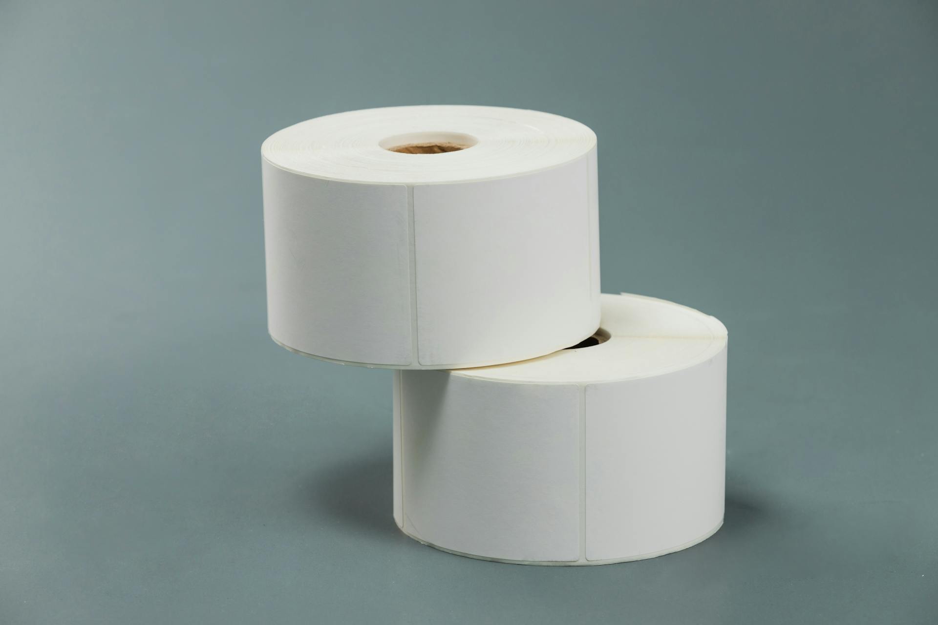 A minimalist composition of two white paper rolls stacked against a grey backdrop.