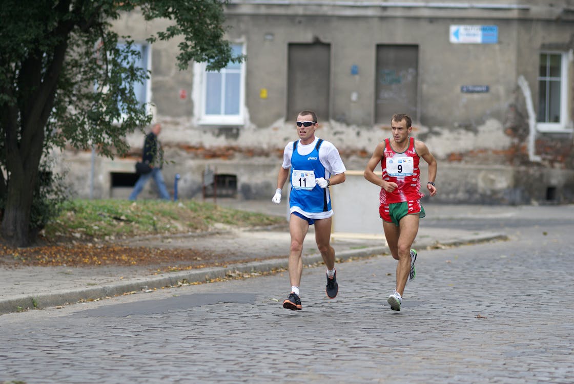 Two men running in a race on a cobblestone street · Free Stock Photo