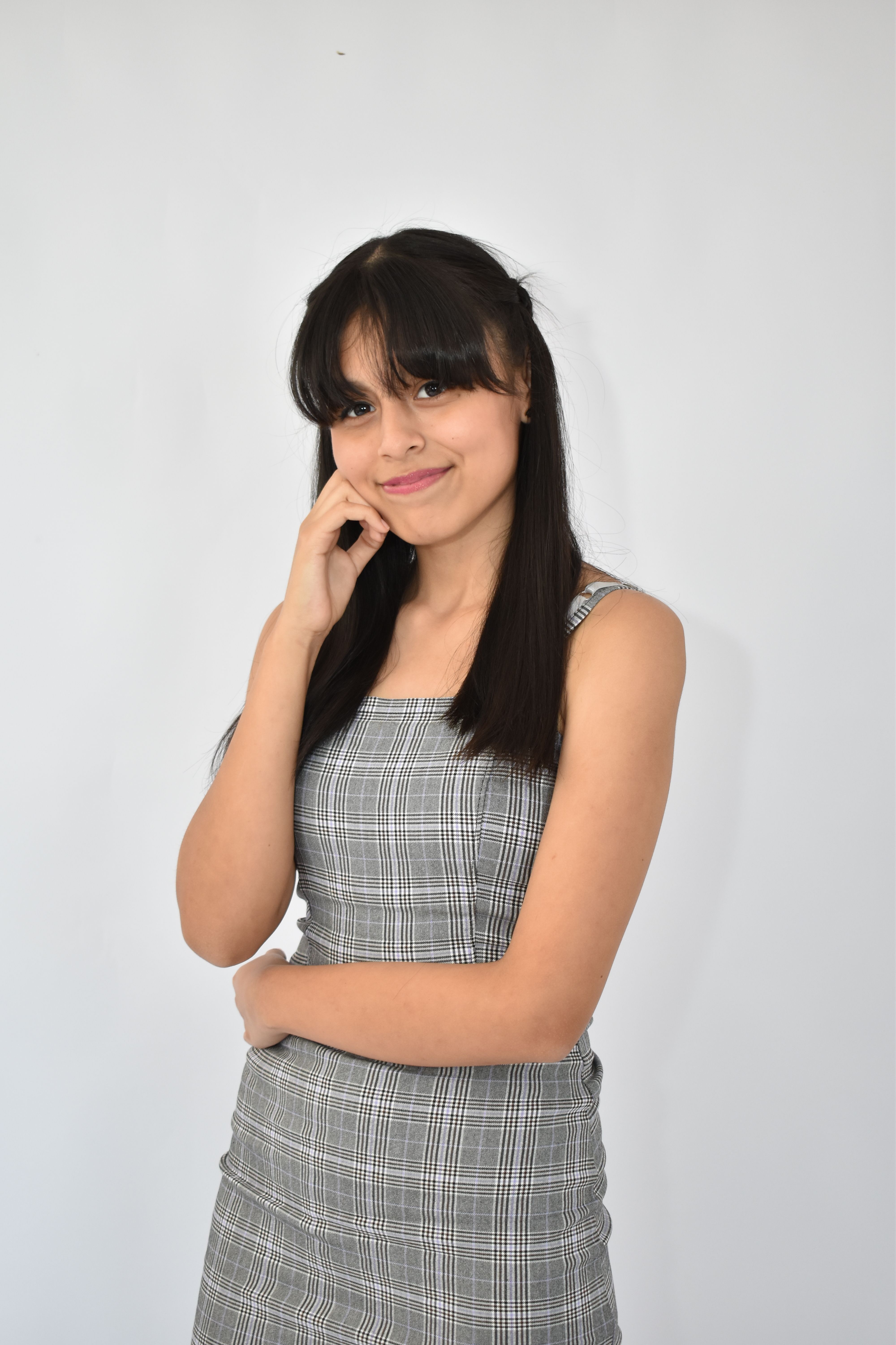 Young woman in a gray dress poses confidently against a plain background, exuding charm and elegance.