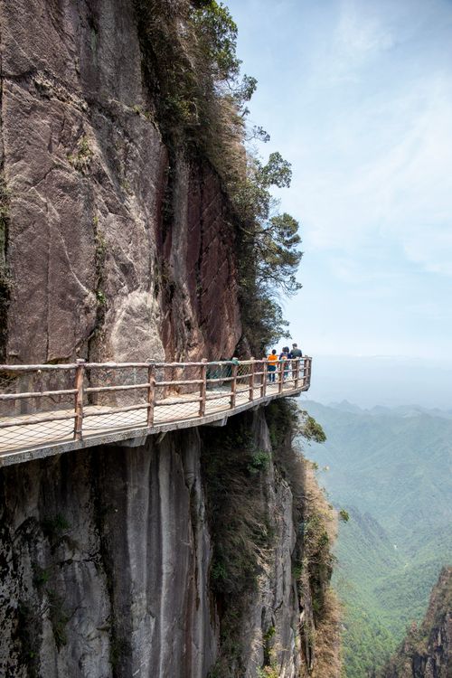 Free A breathtaking view of a footbridge along a sheer cliff with travelers enjoying the mountainous scenery. Stock Photo