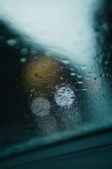 Close-up of raindrops on a glass window with blurred lights in the background creating a moody atmosphere.