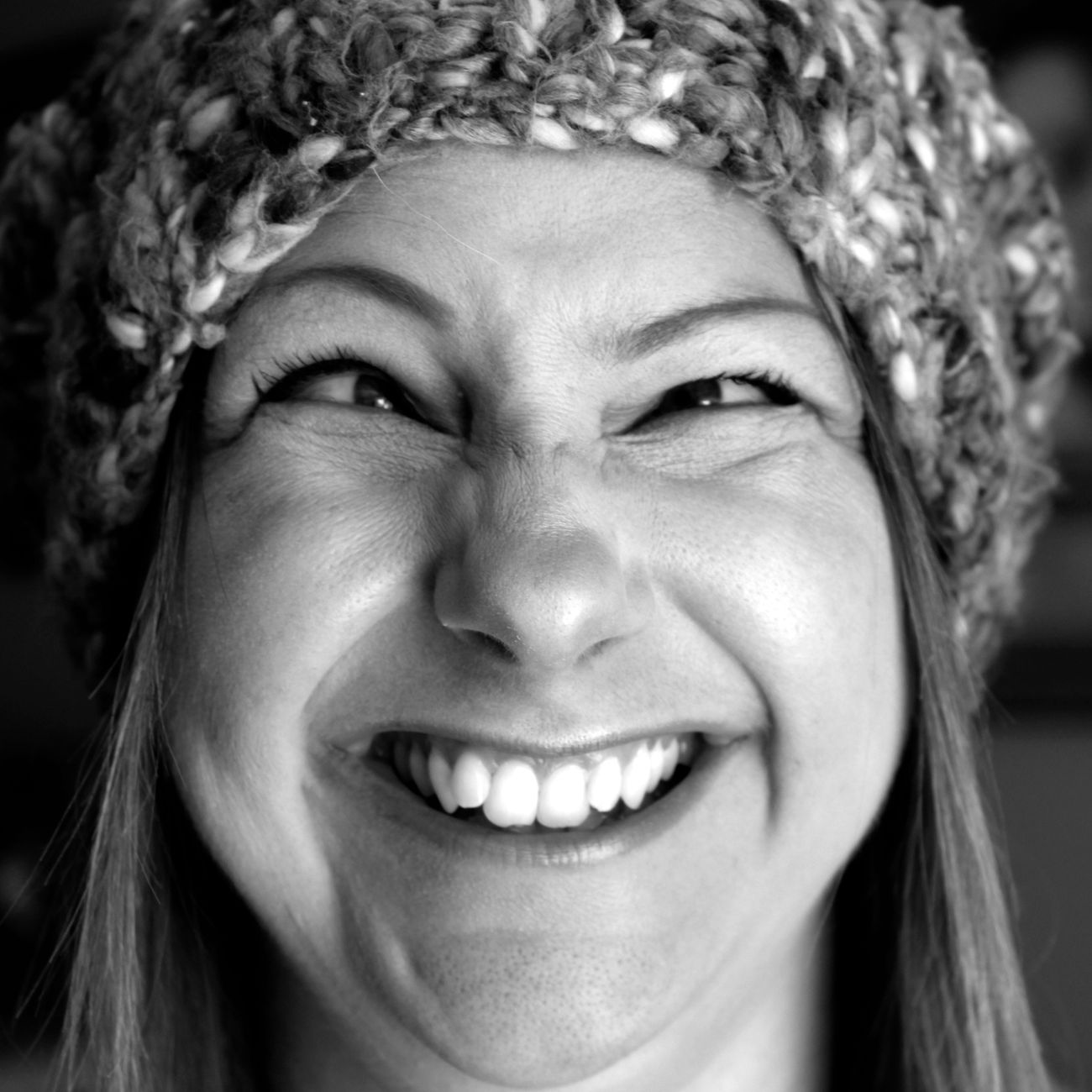 Close-up black and white portrait of a smiling woman in a knit hat showing a joyful expression.