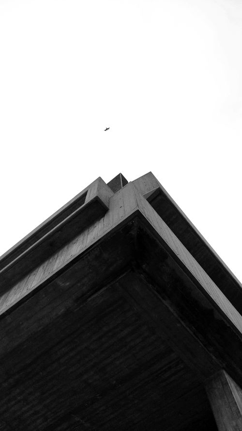 Free High contrast black and white shot of a geometric building design with a plane overhead. Stock Photo