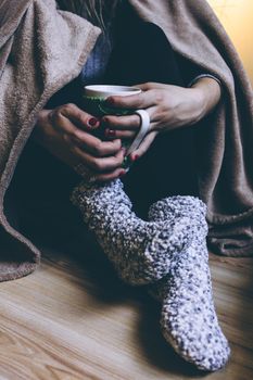 Woman in warm socks and blanket holding a hot drink, creating a cozy ambiance.