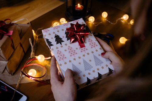 Free Christmas gift with red bow surrounded by glowing string lights, evoking a festive atmosphere. Stock Photo