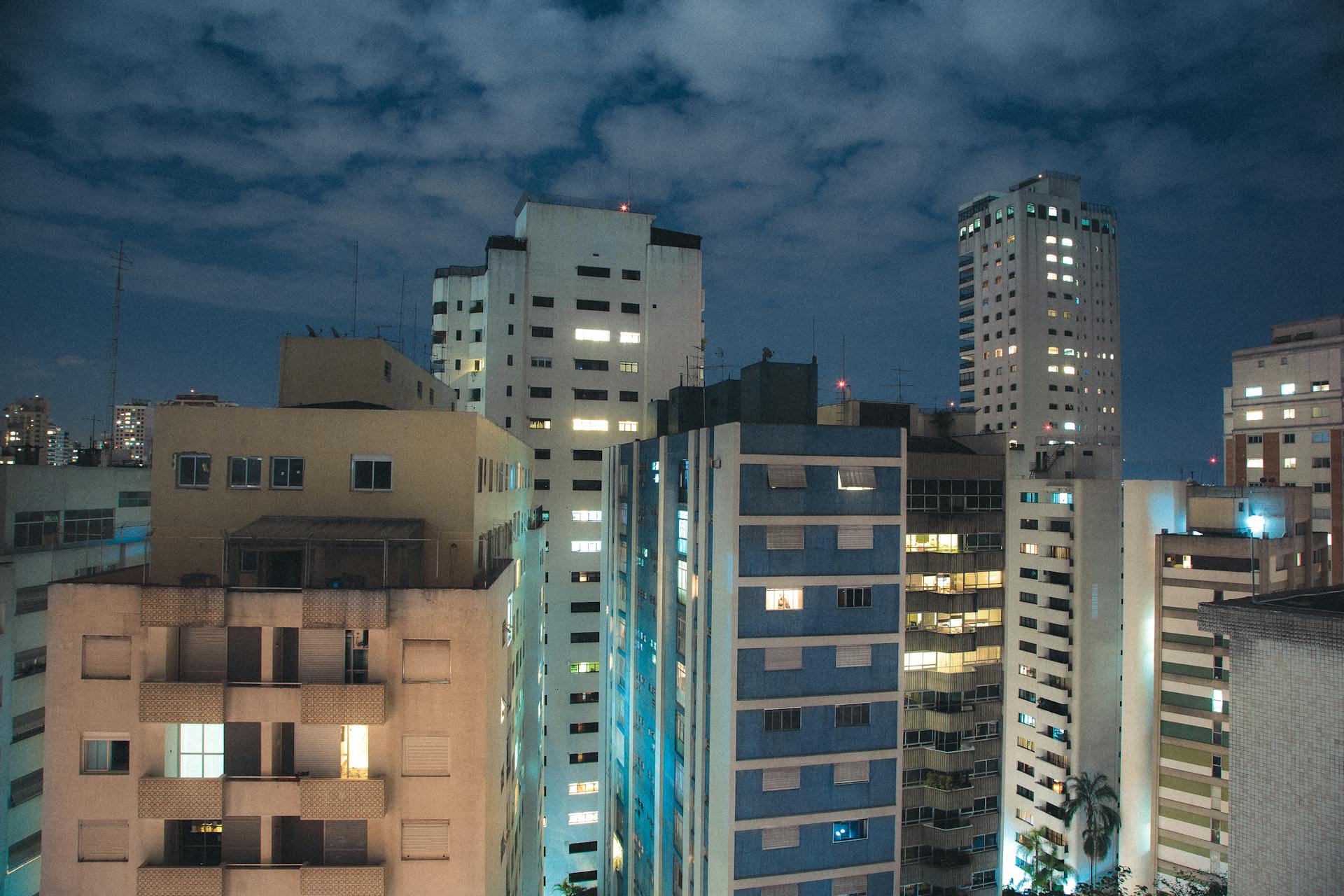 Urban skyline at night featuring illuminated apartment buildings under a clouded sky.