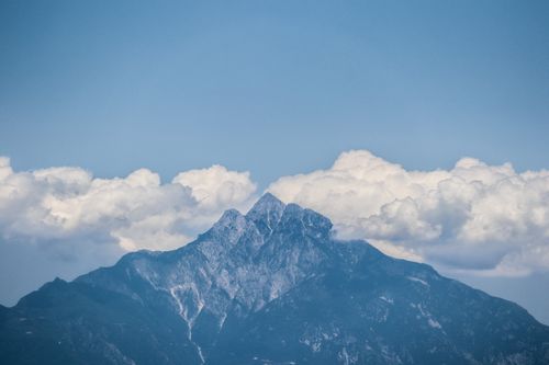 Free A breathtaking view of a rugged mountain peak surrounded by fluffy clouds under a clear blue sky. Stock Photo