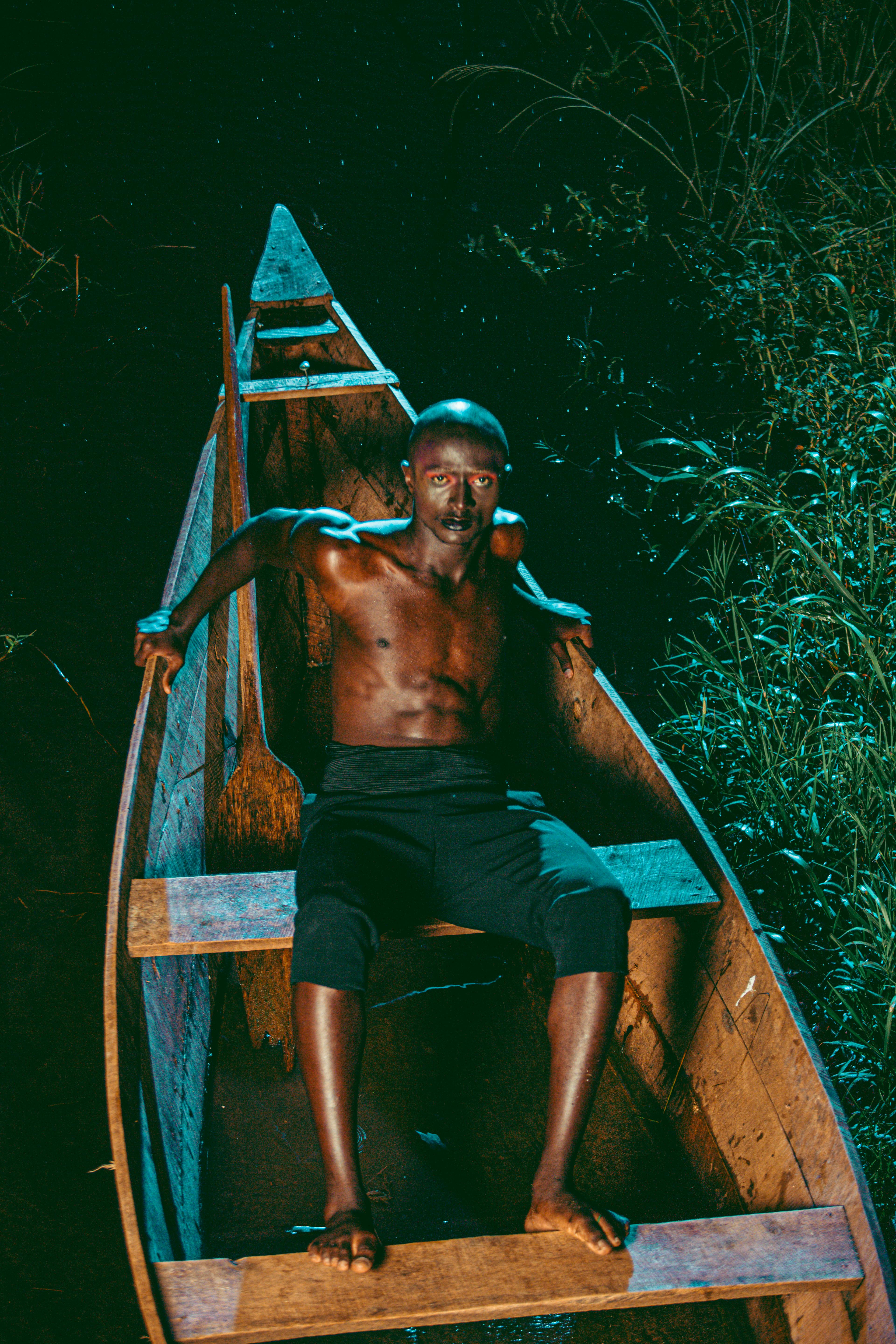 A man sitting in a wooden canoe on a wetland at night, illuminated by soft lighting.