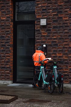 Delivery cyclist with helmet at modern city building entrance with bicycles in view.