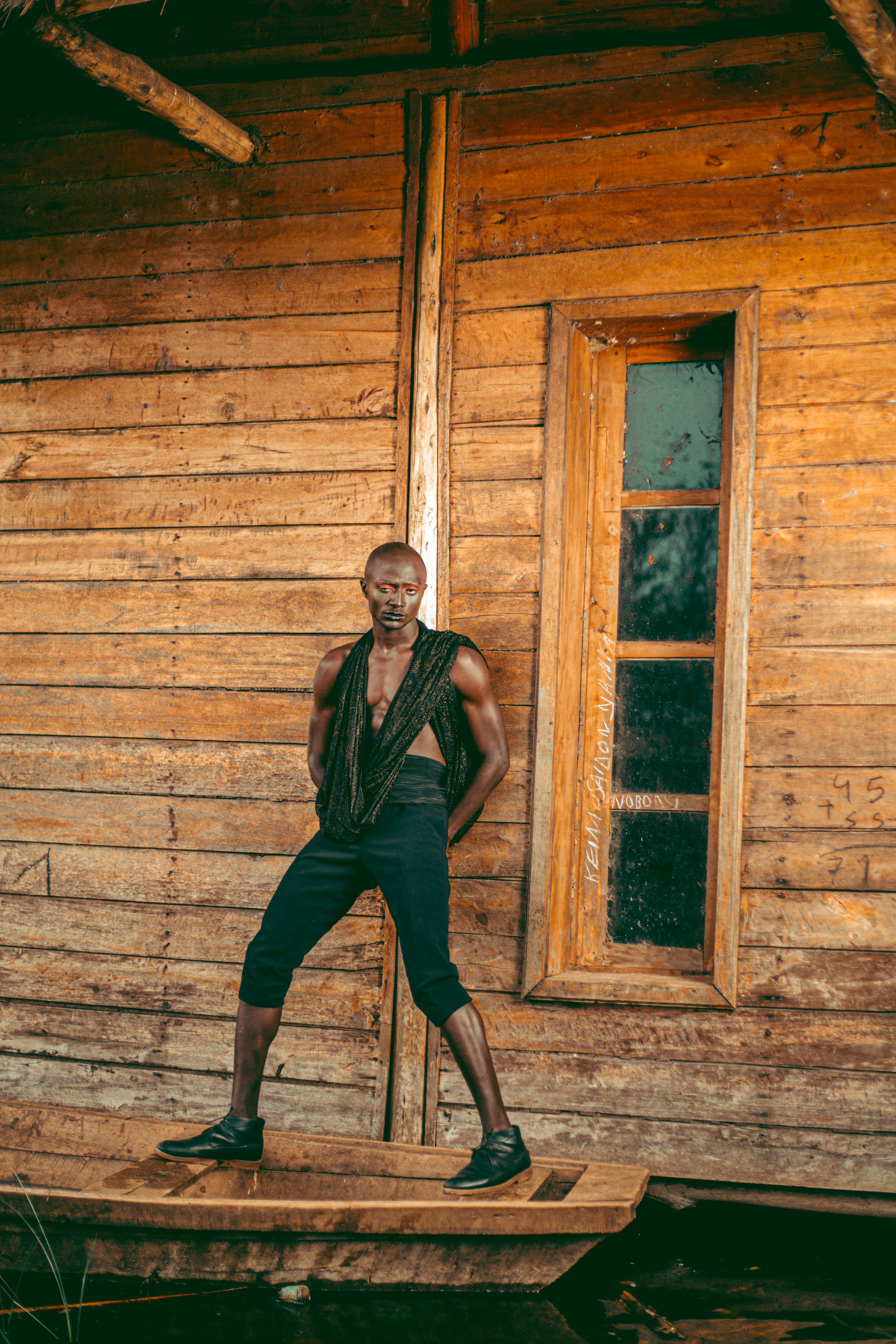 A man standing confidently against a rustic wooden wall, exhibiting modern fashion style.