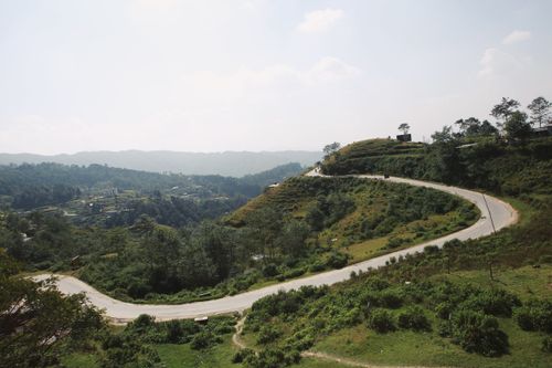 Free A picturesque winding road meanders through lush green hills under a clear blue sky. Stock Photo