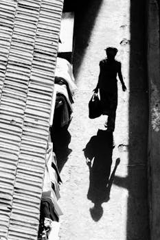 这是一张黑白图像，描绘了一名妇女走在阳光明媚的城市街道上的轮廓