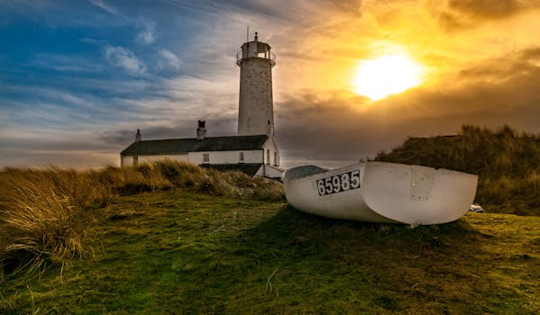 日落时分，灯塔与船只的壮丽景色，映衬着天空的壮观与海岸的草色