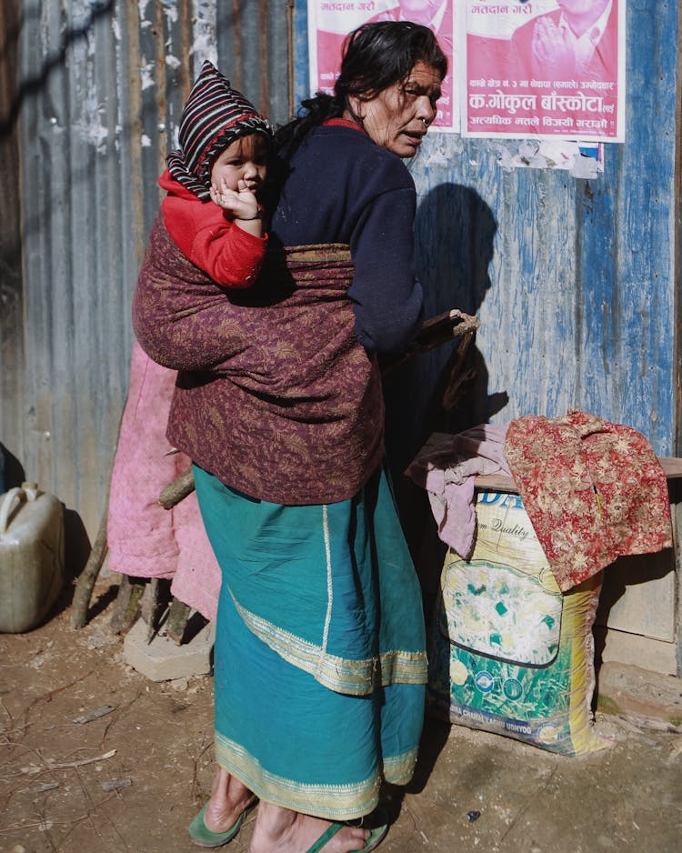 Woman With Child On Back In Poor Village