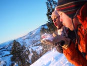 一对穿着冬装的夫妇在风景如画的山上，迎着清澈蔚蓝的天空吹雪