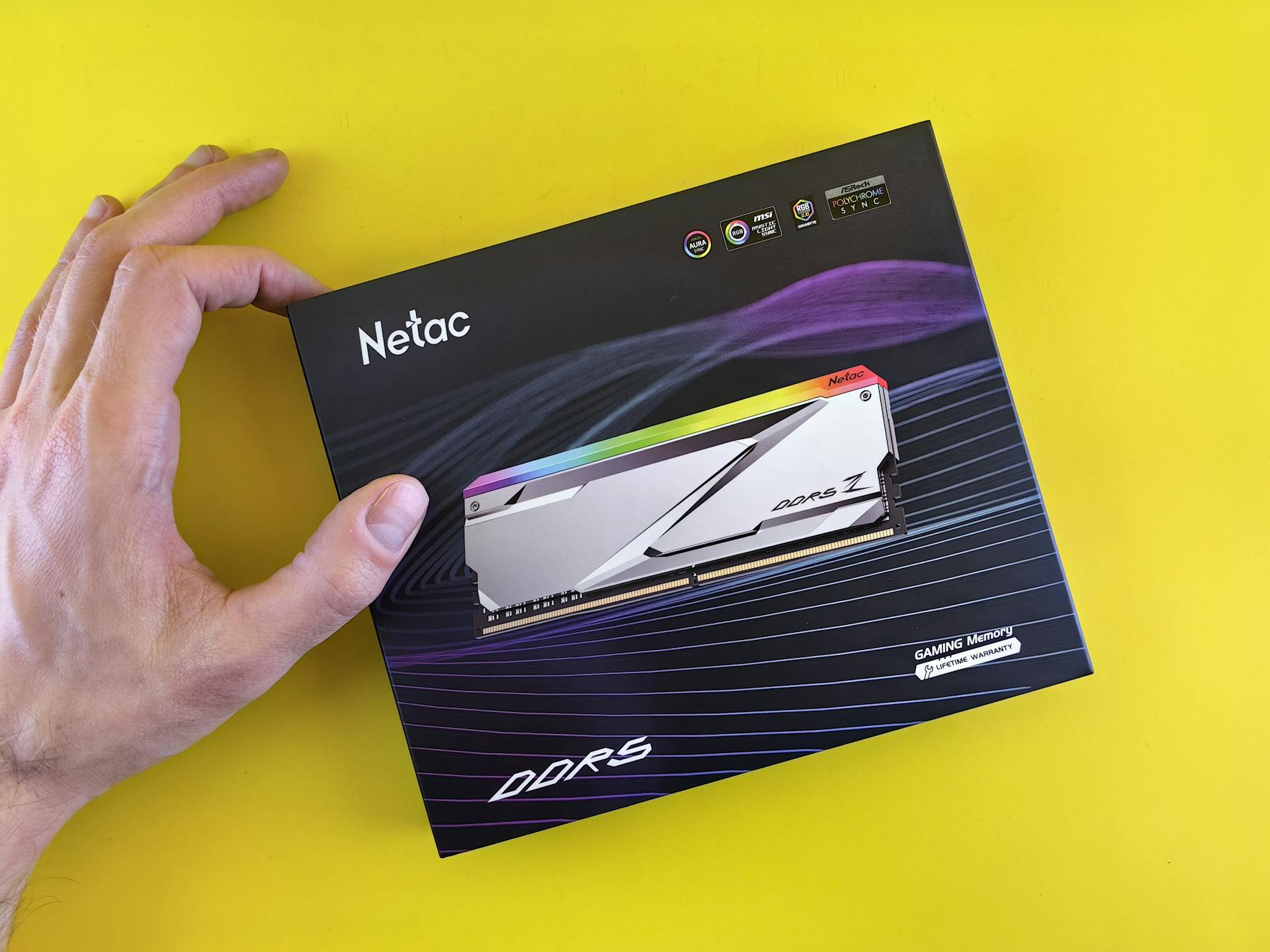 Close-up of a hand holding a Netac DDR5 gaming memory package on a yellow background.