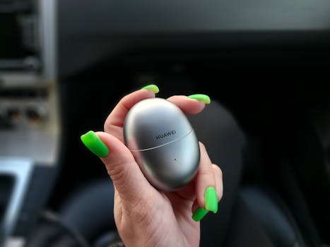 A close-up of a woman's hand holding a wireless earbuds case with green nails.