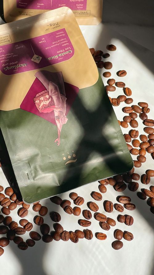 Free A sunlit flat lay of a coffee bag surrounded by scattered coffee beans on a white surface. Stock Photo