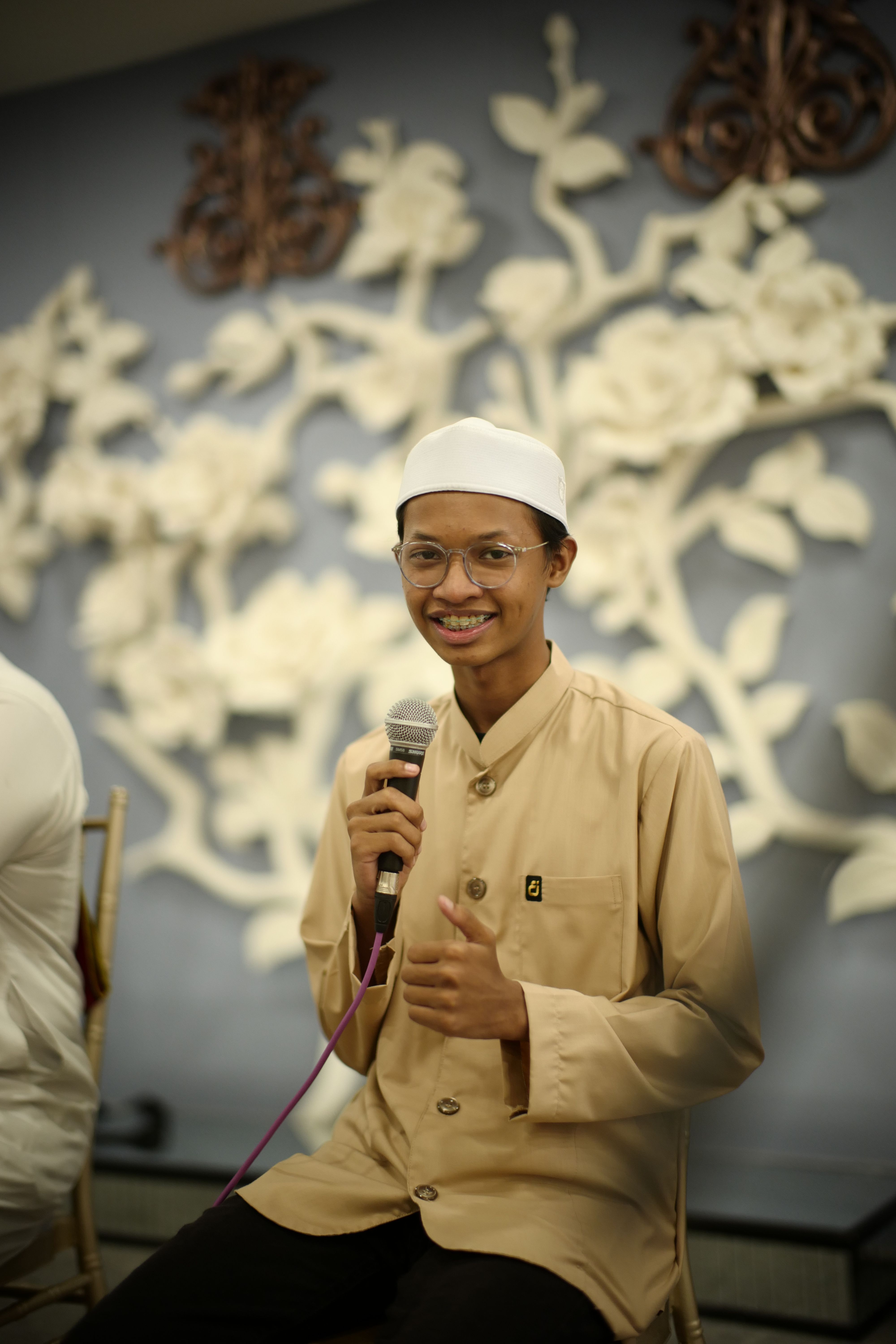 Young Muslim man smiling and holding a microphone indoors in Kuala Lumpur.