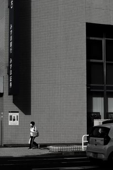 A woman walks past a modern urban building facade in a stark monochrome setting.