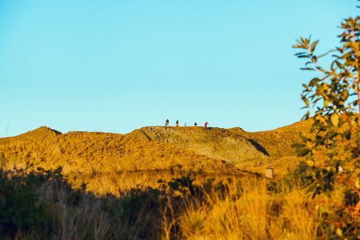 Breathtaking view of hikers on a ridge at sundown, surrounded by golden hills.