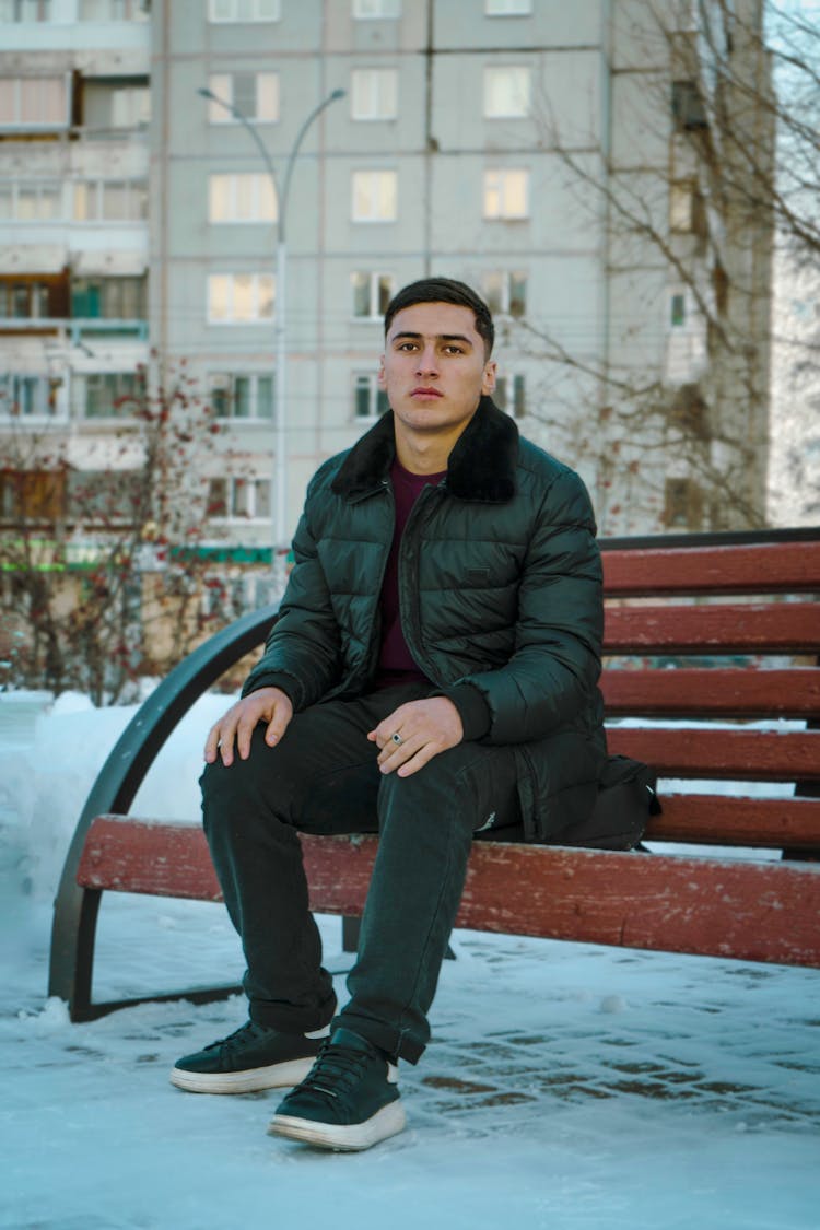 Man In Jacket Sitting On Bench At Park In Winter