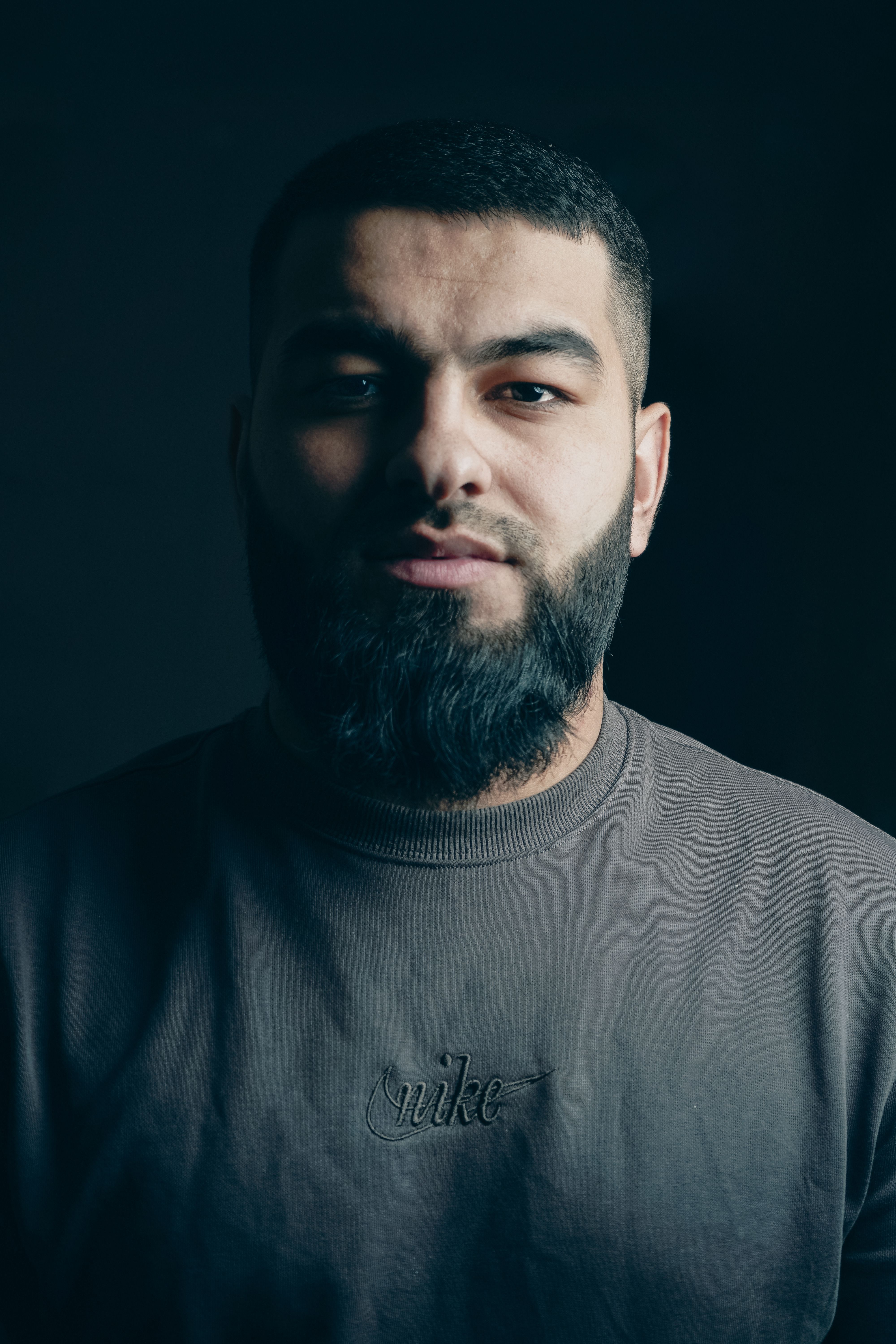 Close-up portrait of a man with a beard against a dark backdrop, in soft lighting.